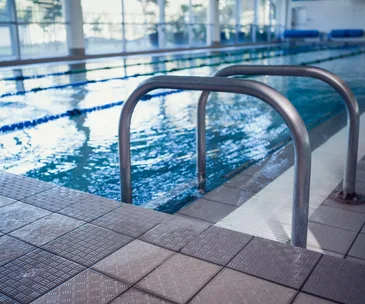 Indoor swimming pool with metal steps, tiled floor, and clear water.