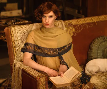 Red-haired person in elegant attire reads a book on a vintage sofa, with a serene dog resting beside.