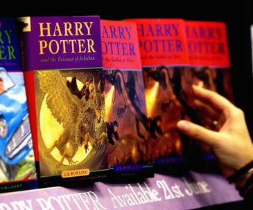 Harry Potter books on a shelf, including "Prisoner of Azkaban," with a person's hand reaching for a book.