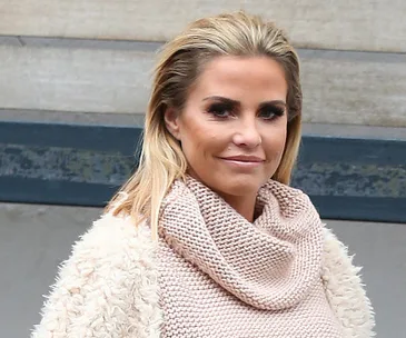 A woman with blonde hair wearing a cream knitted sweater and coat, standing outdoors.