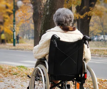 Senior woman in a wheelchair by a tree-lined street in autumn.