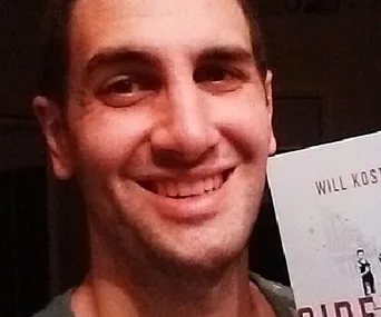 A person smiling while holding a book titled "Side Affects" by Will Kostakis.