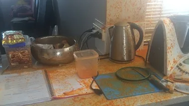 Kitchen counter with food splatter, recipe book, kettle, mixing bowl, and a Thermomix, indicating a cooking mishap.