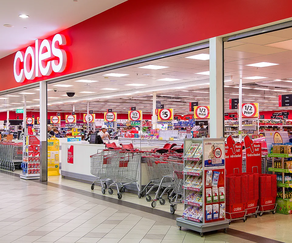 Coles supermarket entrance showing shopping carts, promotional signs, and product displays inside.
