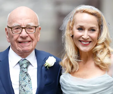 A smiling older couple in wedding attire, with the woman wearing a veil and man in a suit with a rose boutonniere.
