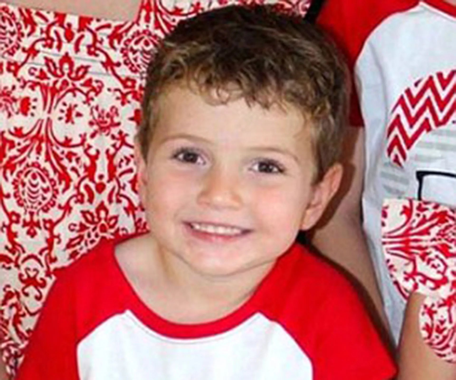 Smiling young boy in a red and white patterned outfit.