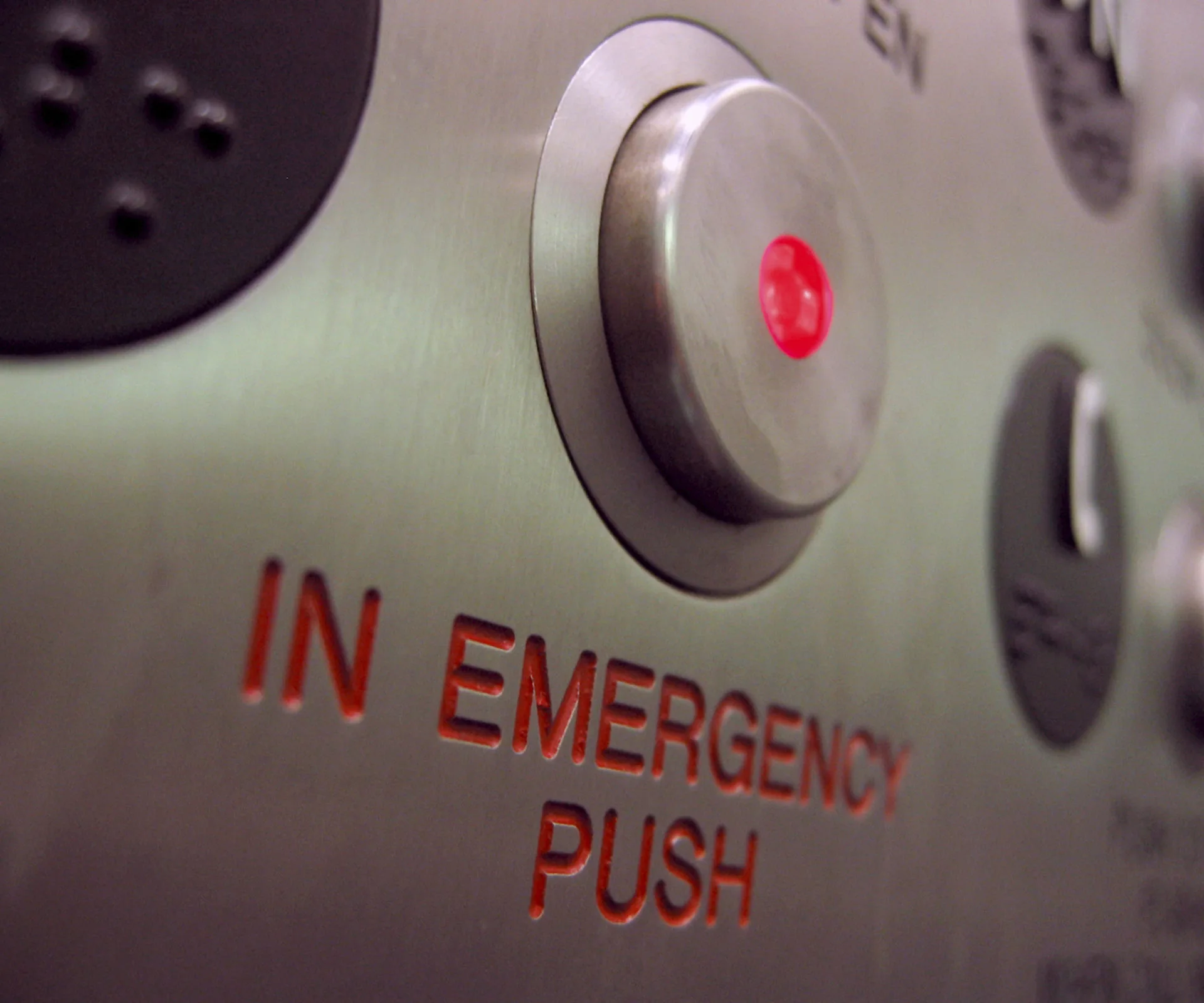 Close-up of an elevator emergency button with red light indicator and "IN EMERGENCY PUSH" text.