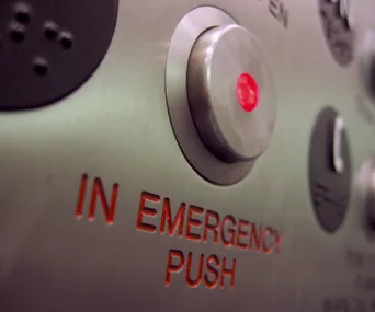 Close-up of an elevator emergency button with red light indicator and "IN EMERGENCY PUSH" text.