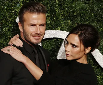 A stylish couple poses at a formal event with greenery and textured elements in the background.