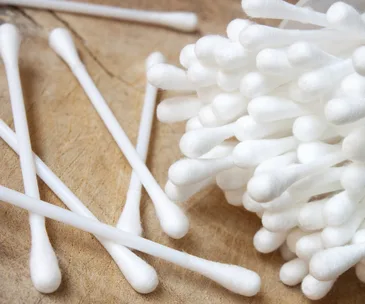Cotton buds on a wooden surface, highlighting their soft, fluffy tips.