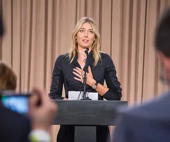 Maria Sharapova at a podium, addressing the media during a press conference with reporters in the foreground.