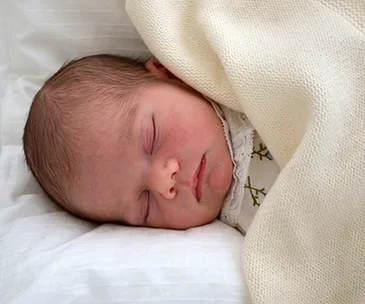 Sleepy newborn Prince Oscar swaddled in a soft cream blanket.