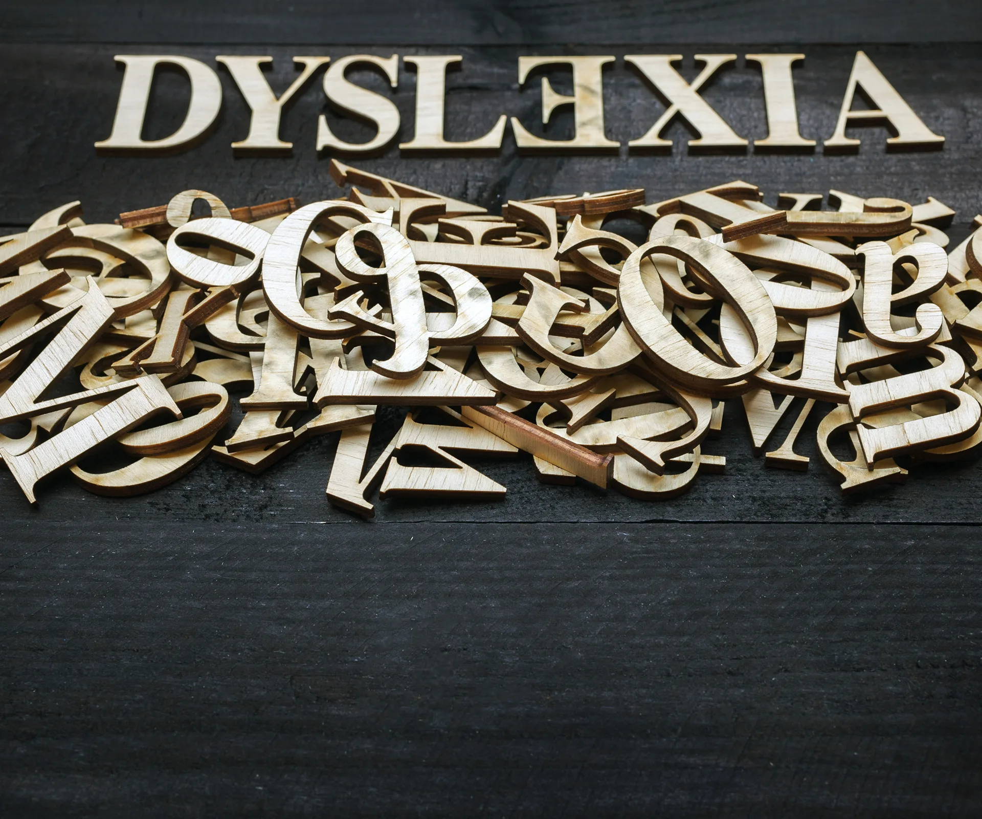 "Pile of wooden letters with 'Dyslexia' spelled out at the top, illustrating difficulty in reading."