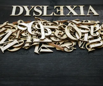 "Pile of wooden letters with 'Dyslexia' spelled out at the top, illustrating difficulty in reading."