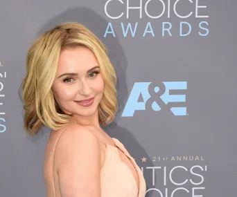 A person in a light peach dress at the Critics' Choice Awards with a branded backdrop.