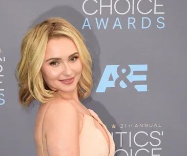 A person in a light peach dress at the Critics' Choice Awards with a branded backdrop.