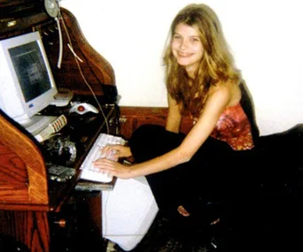 A young girl smiles while using a desktop computer at a wooden desk.