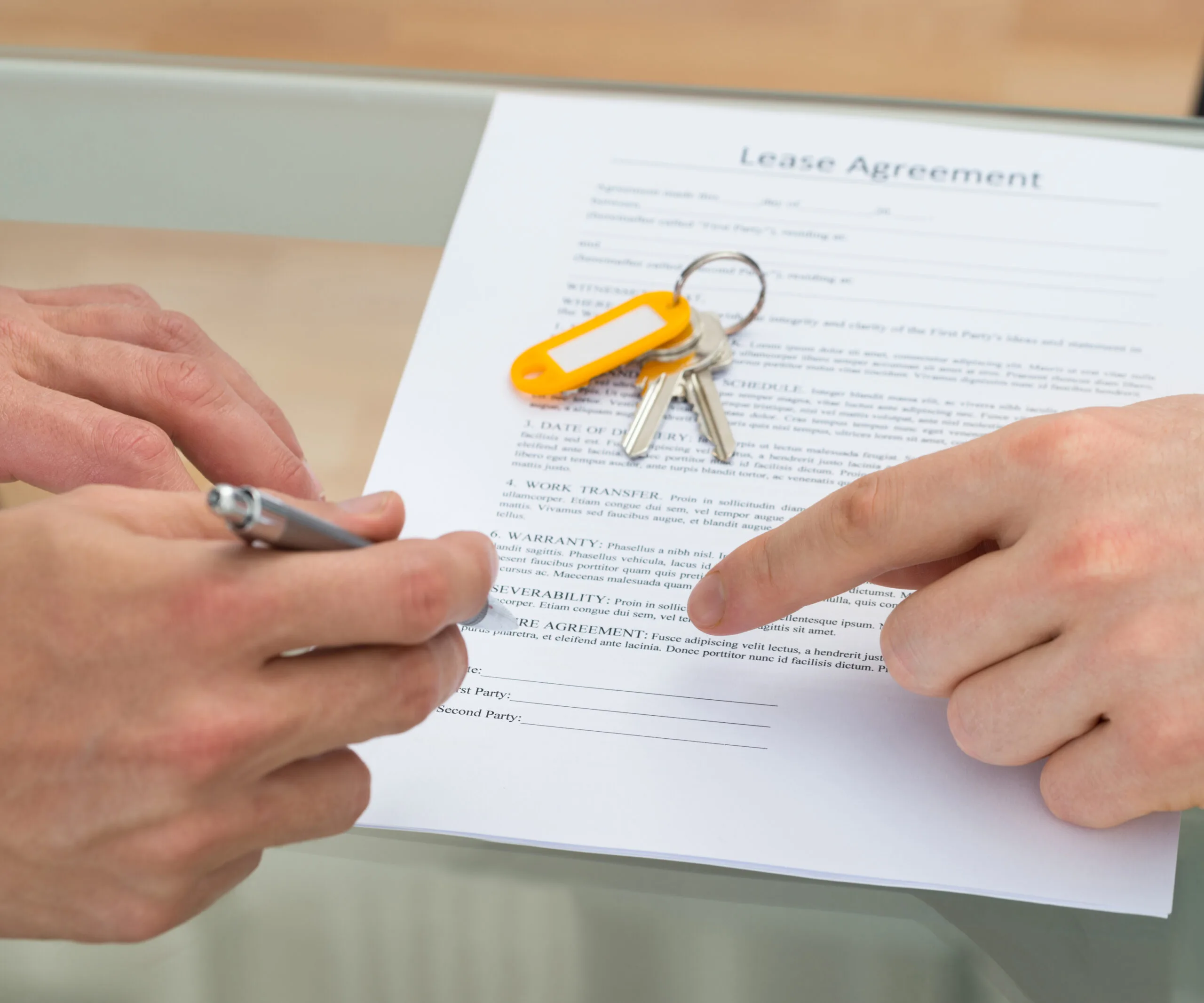 Person signing a lease agreement, with a set of keys and keychain on the table.