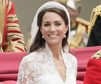 A smiling woman in a lace wedding dress and tiara during a formal outdoor ceremony.