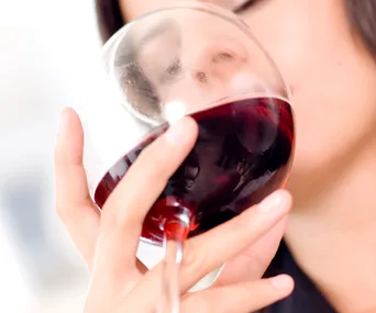 Person sipping red wine from a glass.