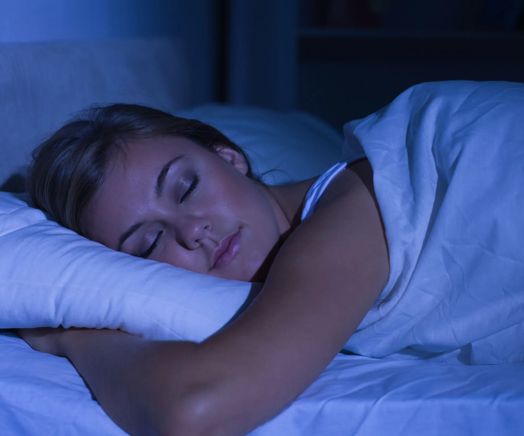A woman sleeping peacefully on her side in a dimly lit room, covered with a white blanket.