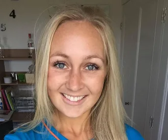 A woman with long blonde hair smiling, indoors, walls with numbers 4 and 5 behind her.