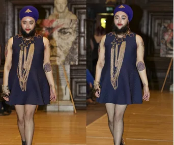 Model on runway wearing blue dress and turban, showcasing a confident walk and unique style.