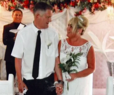 A couple holding hands at their wedding ceremony, smiling at each other.