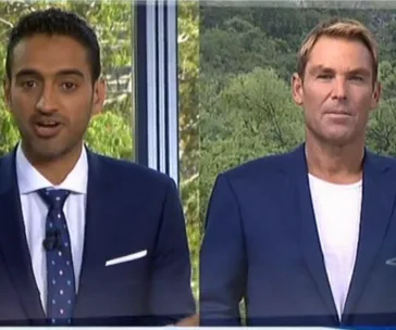 Two men in suits during a televised discussion, standing side by side with a green backdrop.
