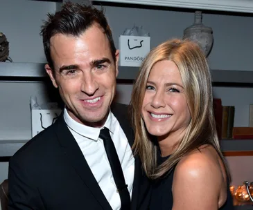 A smiling man in a suit and a woman in a black dress embracing at an event.