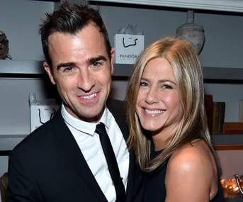 A smiling man in a suit and a woman in a black dress embracing at an event.