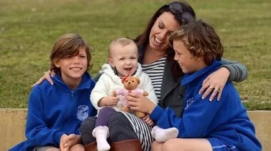 A joyful mother with three children, one toddler holding a teddy bear.