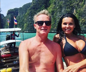 A couple on a boat in Thailand, with cliffs and water in the background, the woman wearing a black bikini.