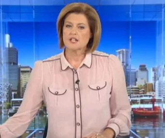 Newsreader in a partially see-through blouse on set; cityscape backdrop.