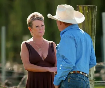 Man in blue shirt and cowboy hat talking to woman in brown dress outdoors.