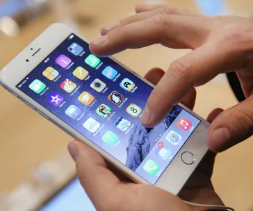 A person using an iPhone with various app icons visible on the screen.