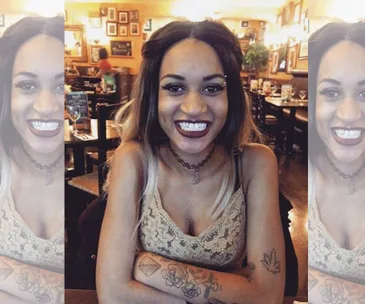 A smiling woman with tattoos, seated at a restaurant, with a blurred background.