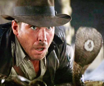 Indiana Jones cautiously faces a cobra, wearing his iconic fedora and leather jacket.