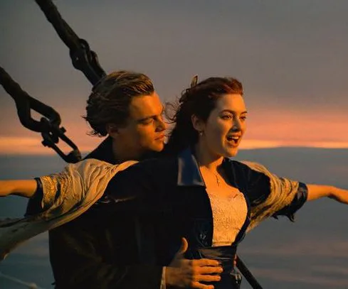 A couple embraces at the bow of a ship at sunset in an iconic scene from a movie.