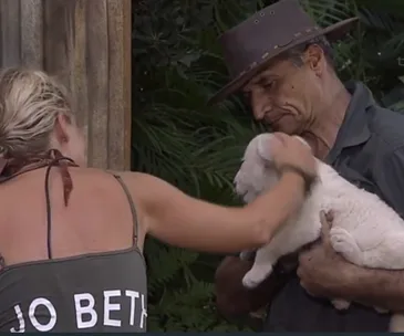 Two people interacting with a white lamb; one holds the lamb while the other strokes it.