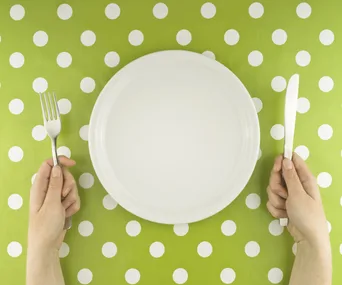Empty plate on green polka dot tablecloth, hands holding fork and knife.