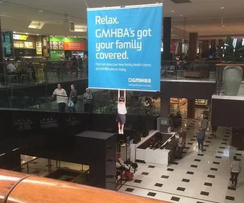 Child mannequin hanging from a GMHBA advertisement in Melbourne shopping center, alarming shoppers below.