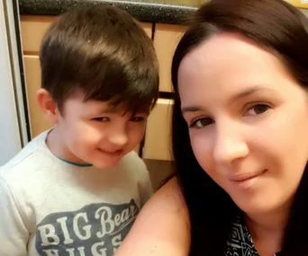 A woman and a young child smiling in a kitchen setting.