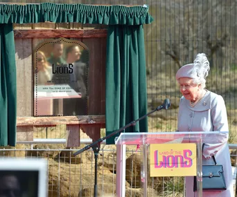 "Queen Elizabeth II at Land of the Lions exhibit unveiling, standing by a plaque with green curtains, 2016."