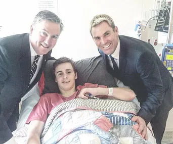 Three men, including one in a hospital bed, smiling together in a hospital room.