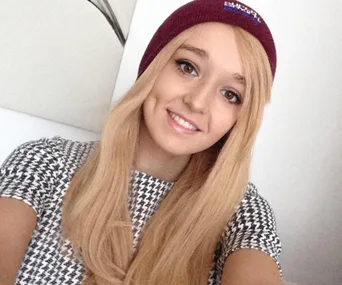 A young woman with long blonde hair and a maroon beanie smiles at the camera.