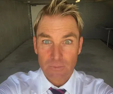 A man with tousled blonde hair and a surprised expression takes a selfie in a concrete room.