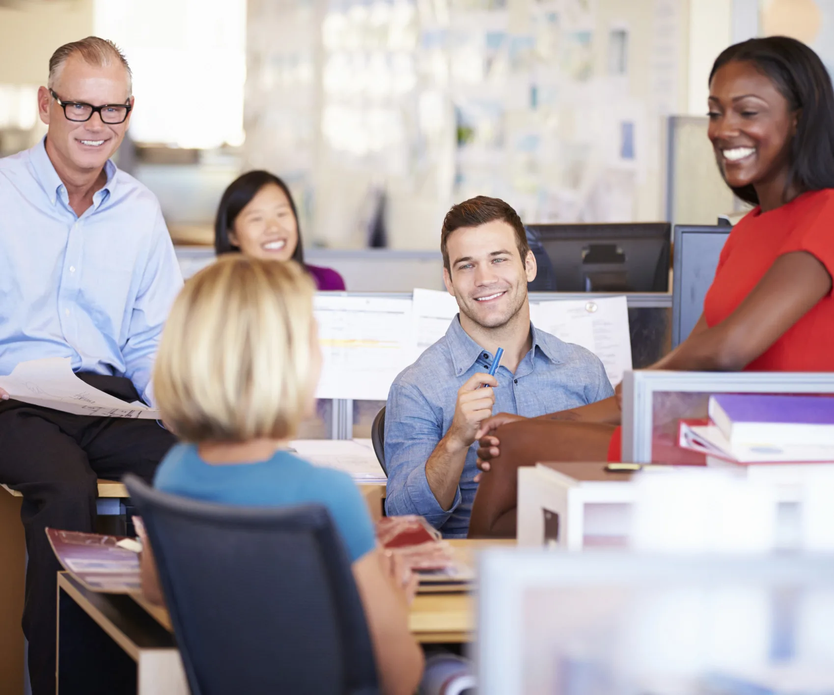 Group of diverse coworkers smiling and interacting in a modern office setting.