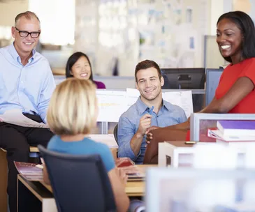 Group of diverse coworkers smiling and interacting in a modern office setting.