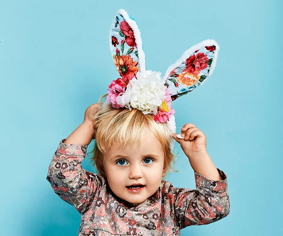 Child wearing floral bunny ears headband against blue background.